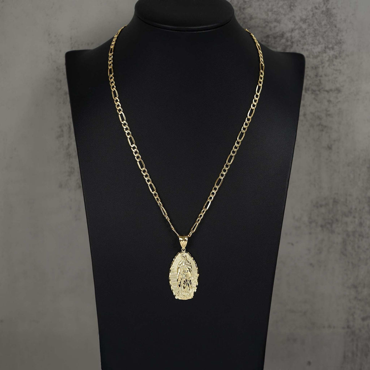 Gold Our Lady of Guadalupe oval pendant necklace on a figaro chain displayed on a black neck bust.