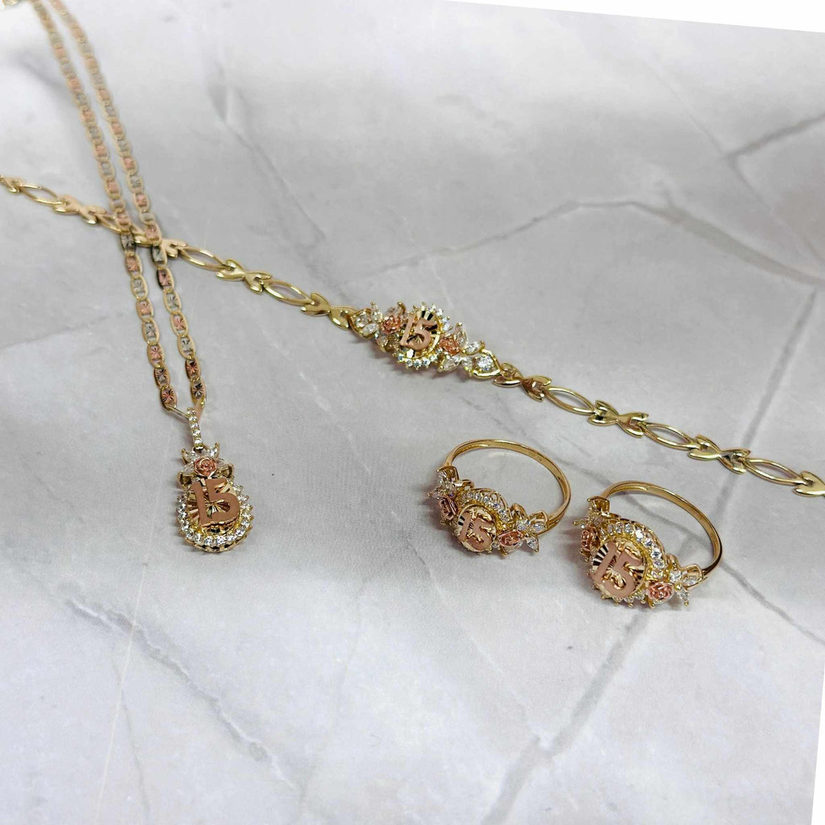 Two-tone gold quinceañera jewelry set with 15 pendant necklace, bracelet, and two rings.