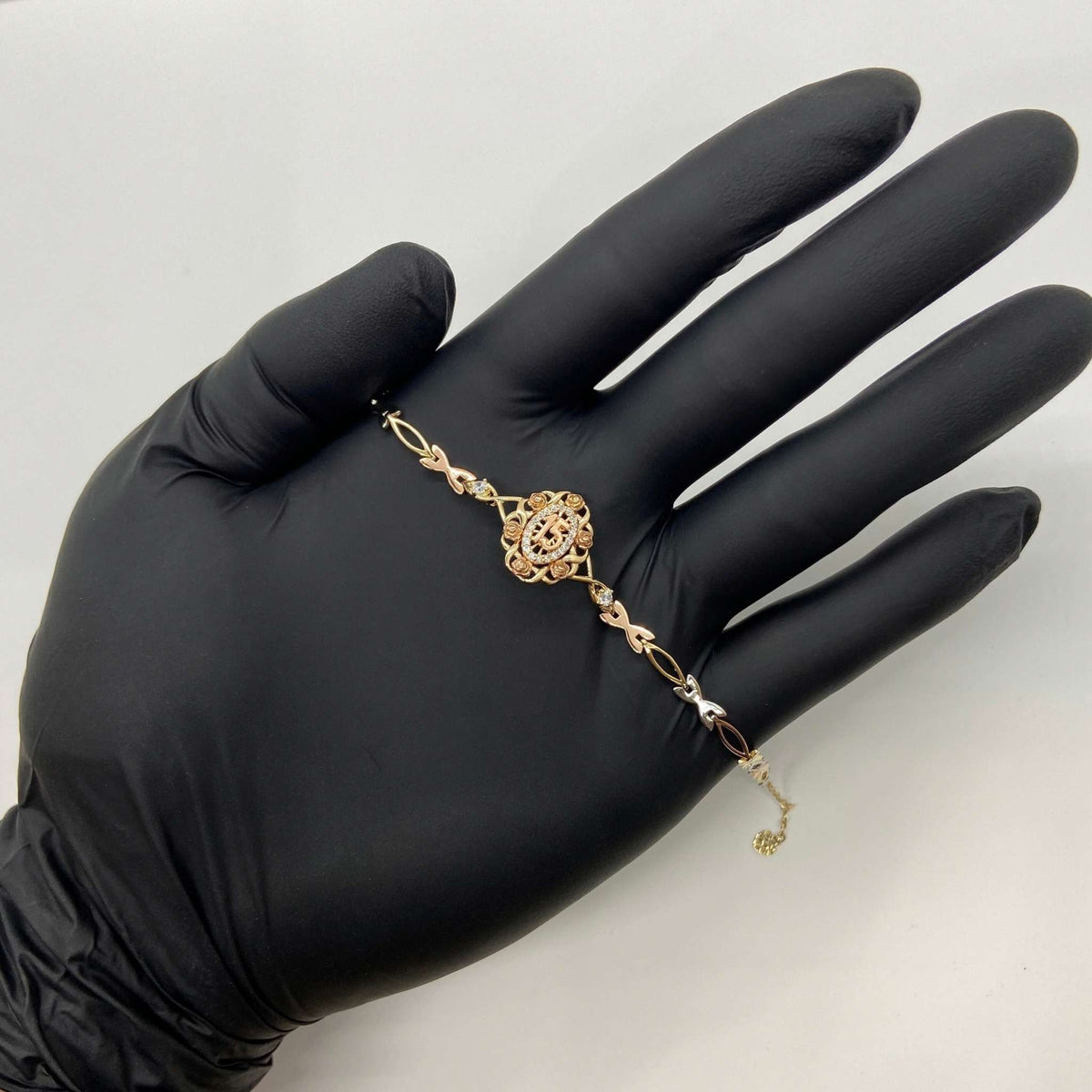 Gold Quinceañera 15th birthday rose motif charm bracelet displayed across an open hand.