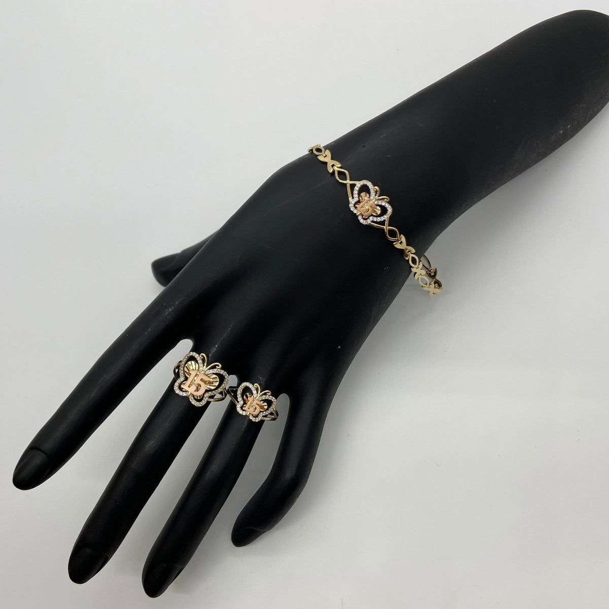 Gold Quinceañera 15 butterfly bracelet and matching ring set displayed on a black mannequin hand.