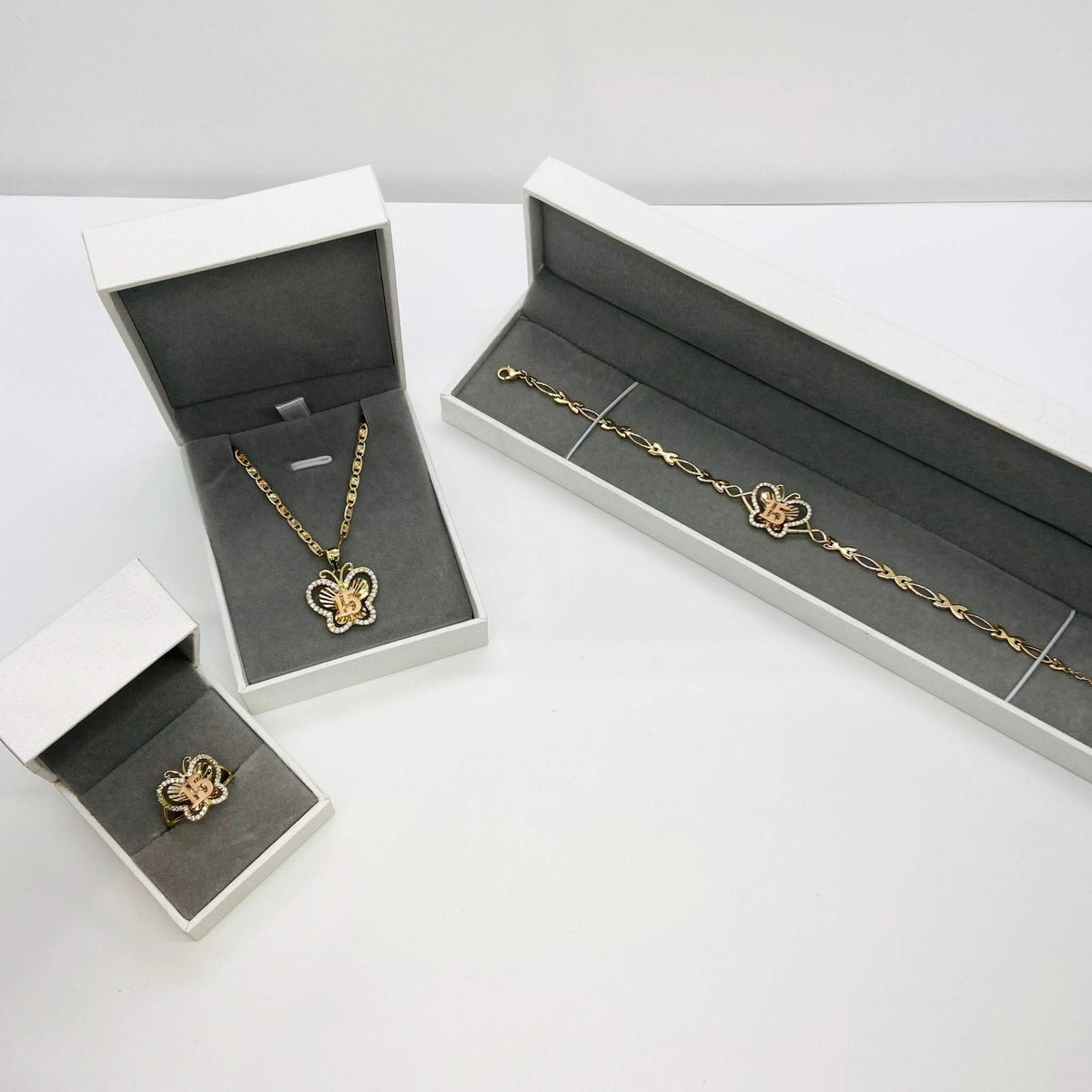 Three-piece gold Quinceañera 15 butterfly jewelry set with CZ accents packaged in white gift boxes.