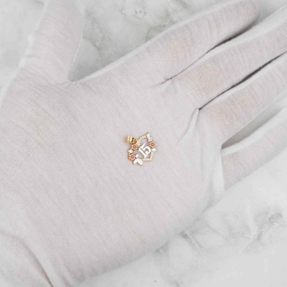 White gloved hand holding a tri-color gold Quinceañera 15 heart pendant.