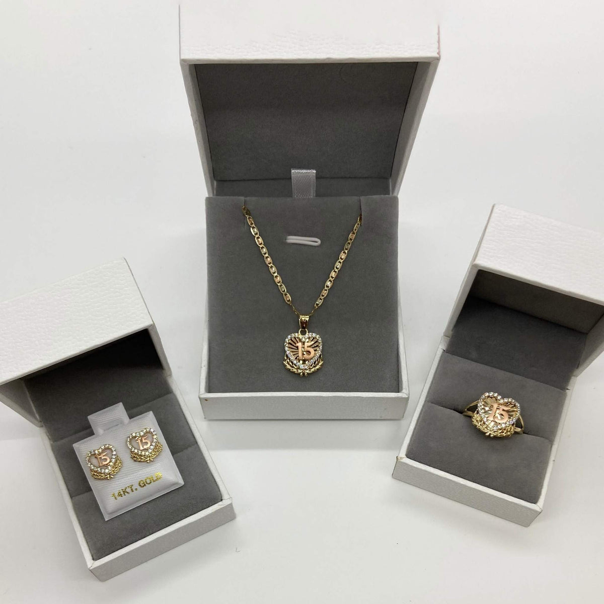 Matching gold Quinceañera 15 jewelry set displaying necklace, ring, and earrings in boxes