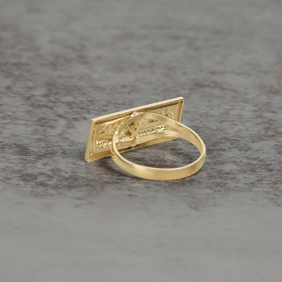Back view of a gold Last Supper signet ring on a gray textured surface.