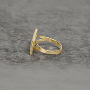 Side view of a two-tone gold Last Supper ring on a gray textured surface.