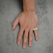 Hand wearing a two-tone gold rectangular ring on a textured gray background.