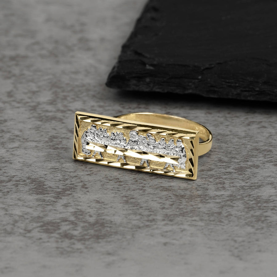 Two-tone gold rectangular ring featuring an engraved Last Supper scene on a dark surface.