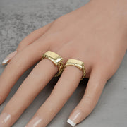 Two gold Cuban link ID rings worn on a hand against a neutral background.