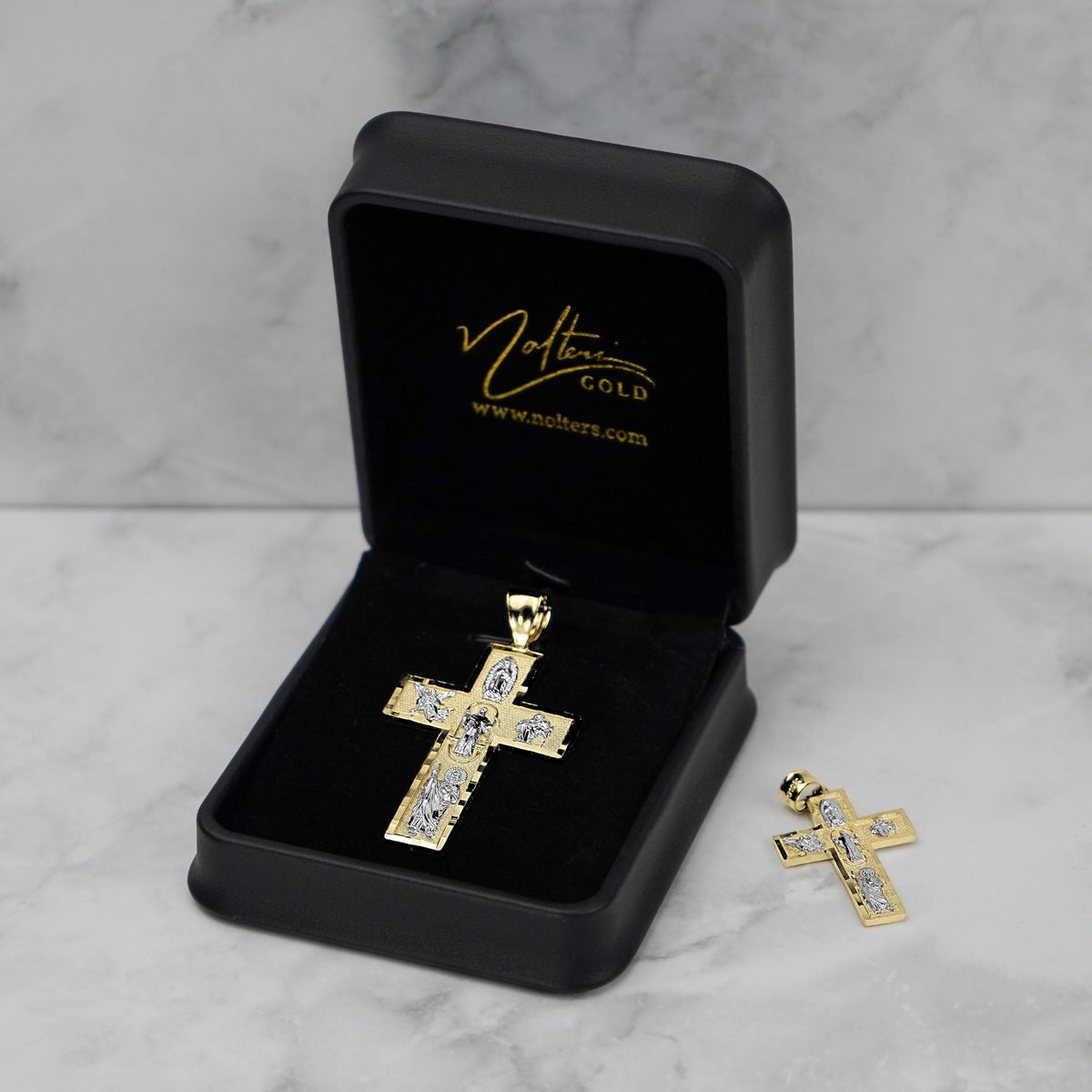 Gold cross pendant in an open black Nolters jewelry box with another pendant beside it.