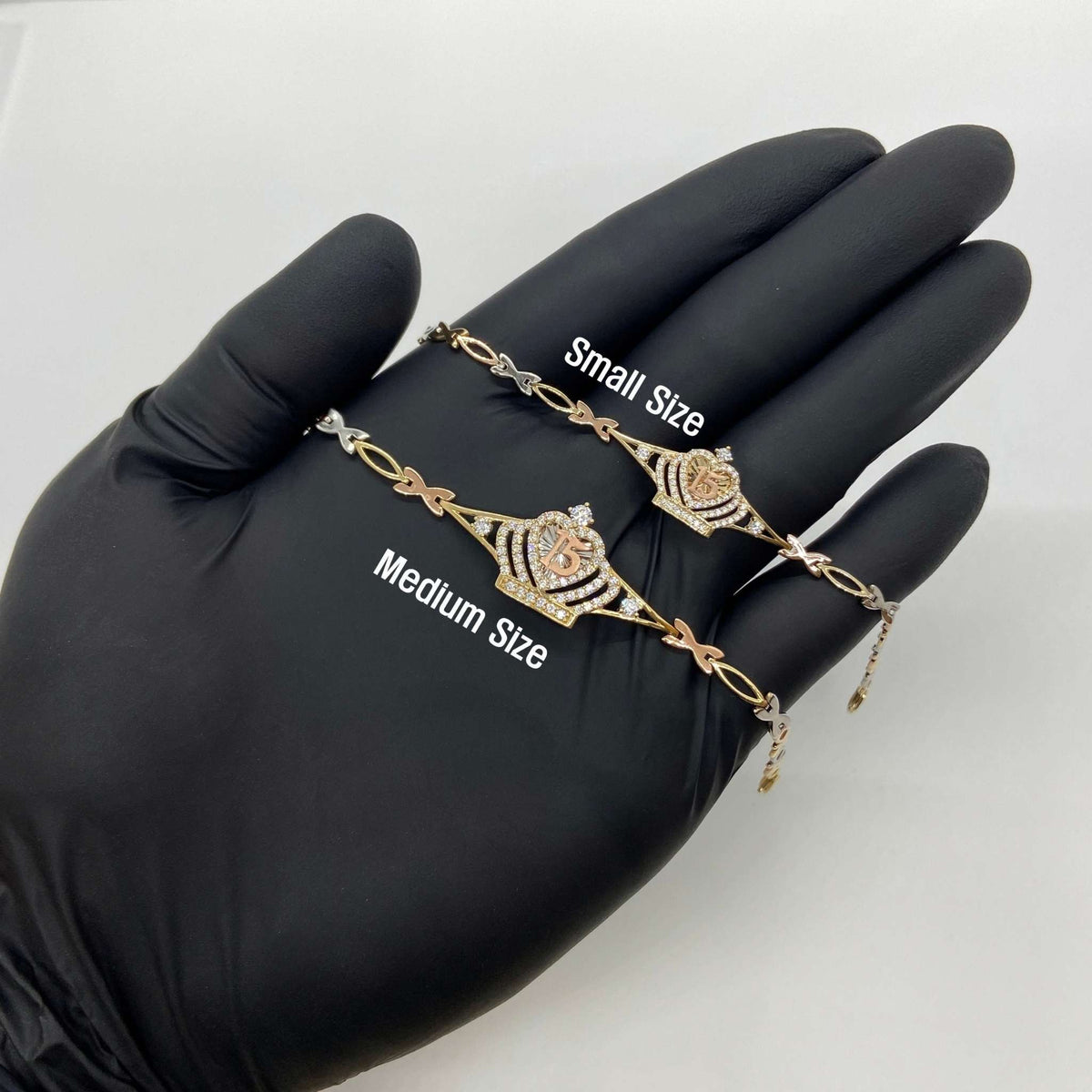 Gloved hand holding small and medium gold Quinceañera crown charm bracelets.