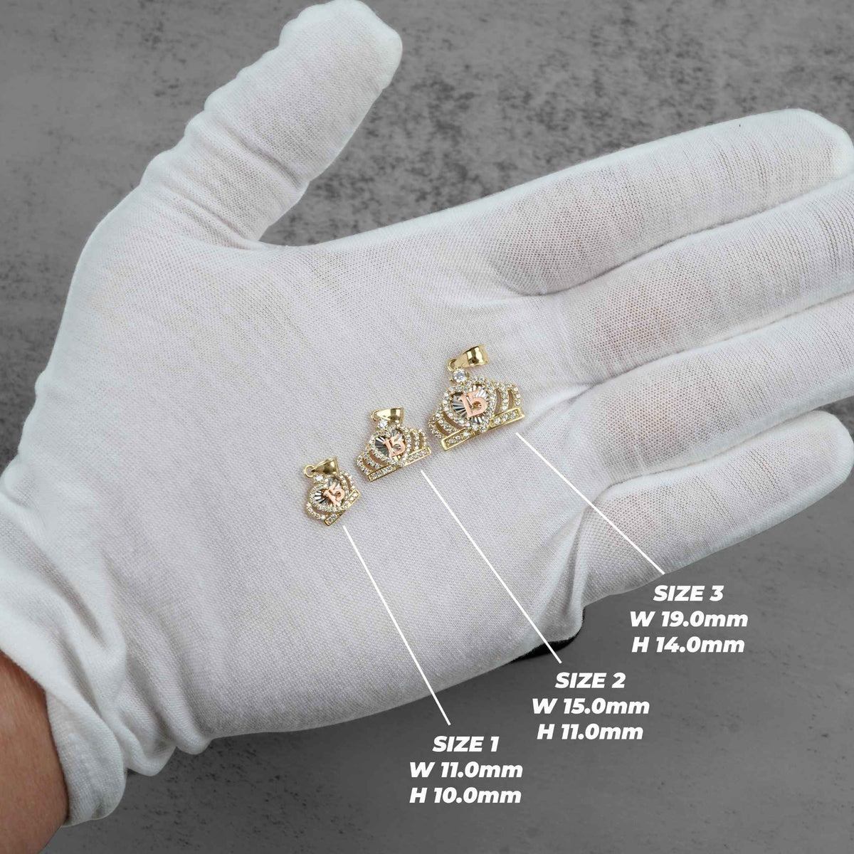 Three labeled sizes of gold Quinceañera royal crown pendants resting on a white gloved hand.