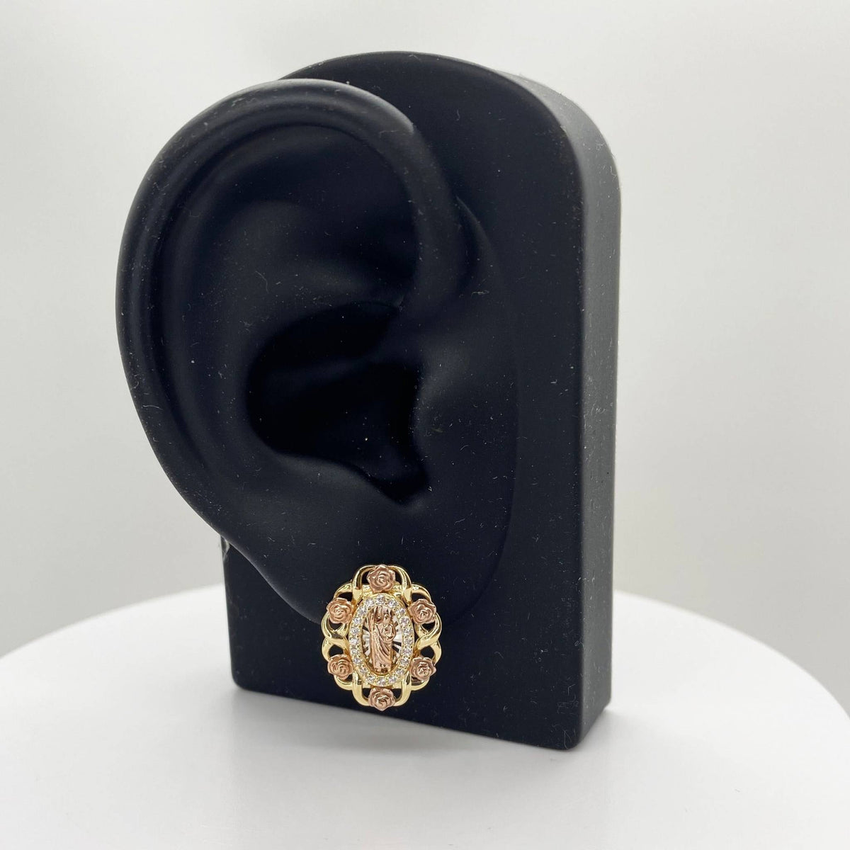 Tri-color gold San Judas oval stud earring displayed on a black mannequin ear stand.