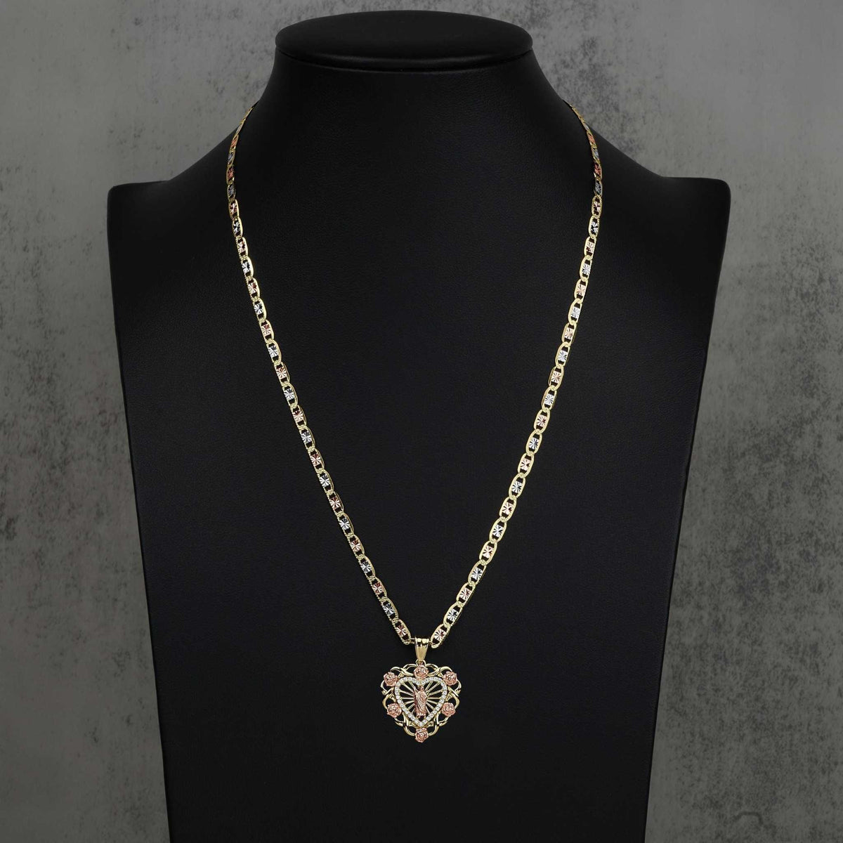 Two-tone gold San Judas heart pendant styled on a tricolor chain over a black mannequin bust.
