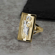 Men's two-tone gold rectangular San Judas signet ring displayed on a textured surface.