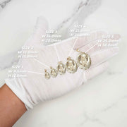 Gloved hand holding five gold Virgin Mary pendants in size order on marble.