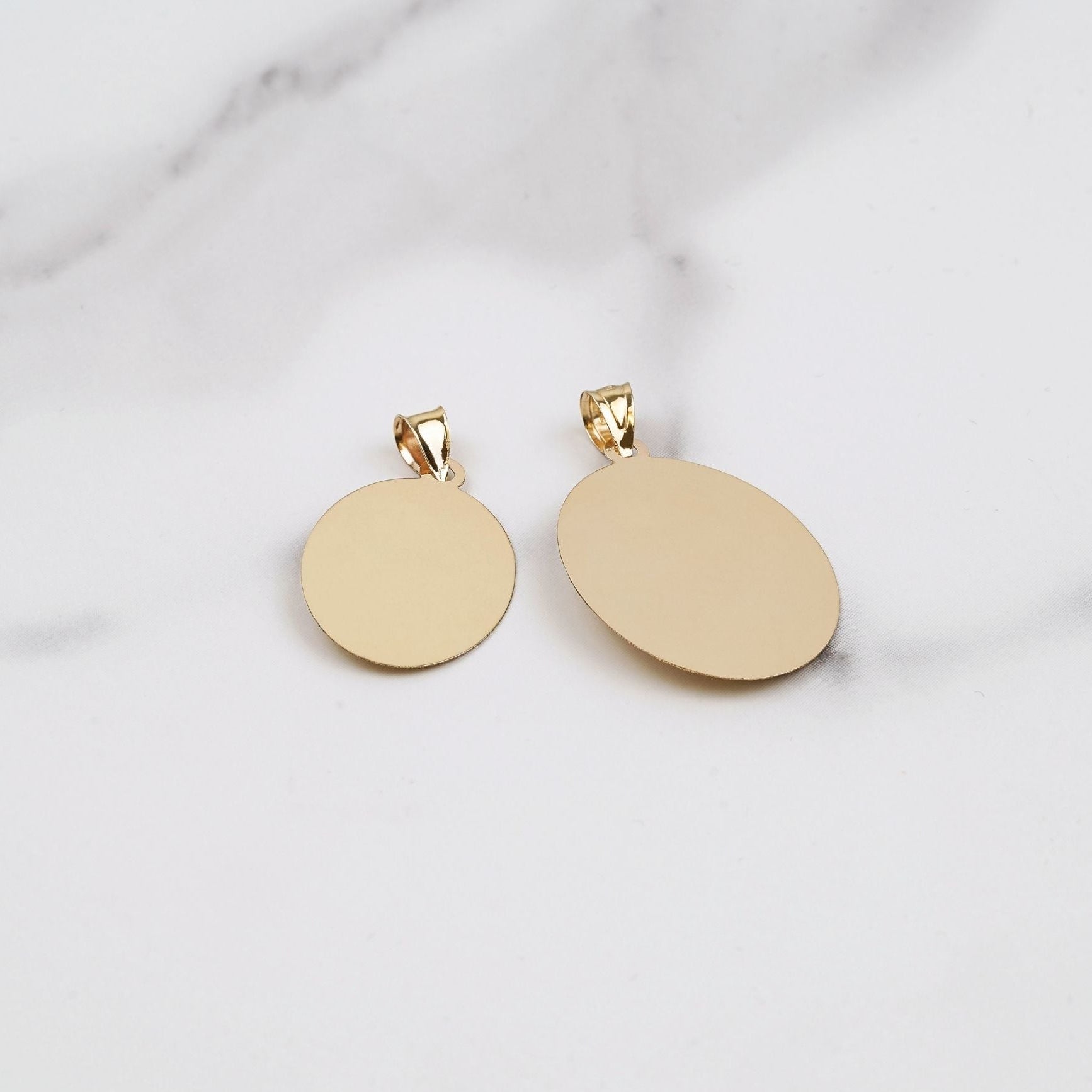 Back view of two smooth yellow gold Virgin Mary oval pendants on marble.
