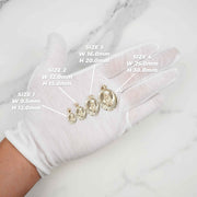 Gloved hand holding yellow gold Virgin Mary oval pendants showing different size options.