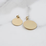 Back view of two plain round yellow gold pendants on a marble surface.