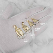 Four gold praying hands pendant sizes displayed on a white gloved hand.