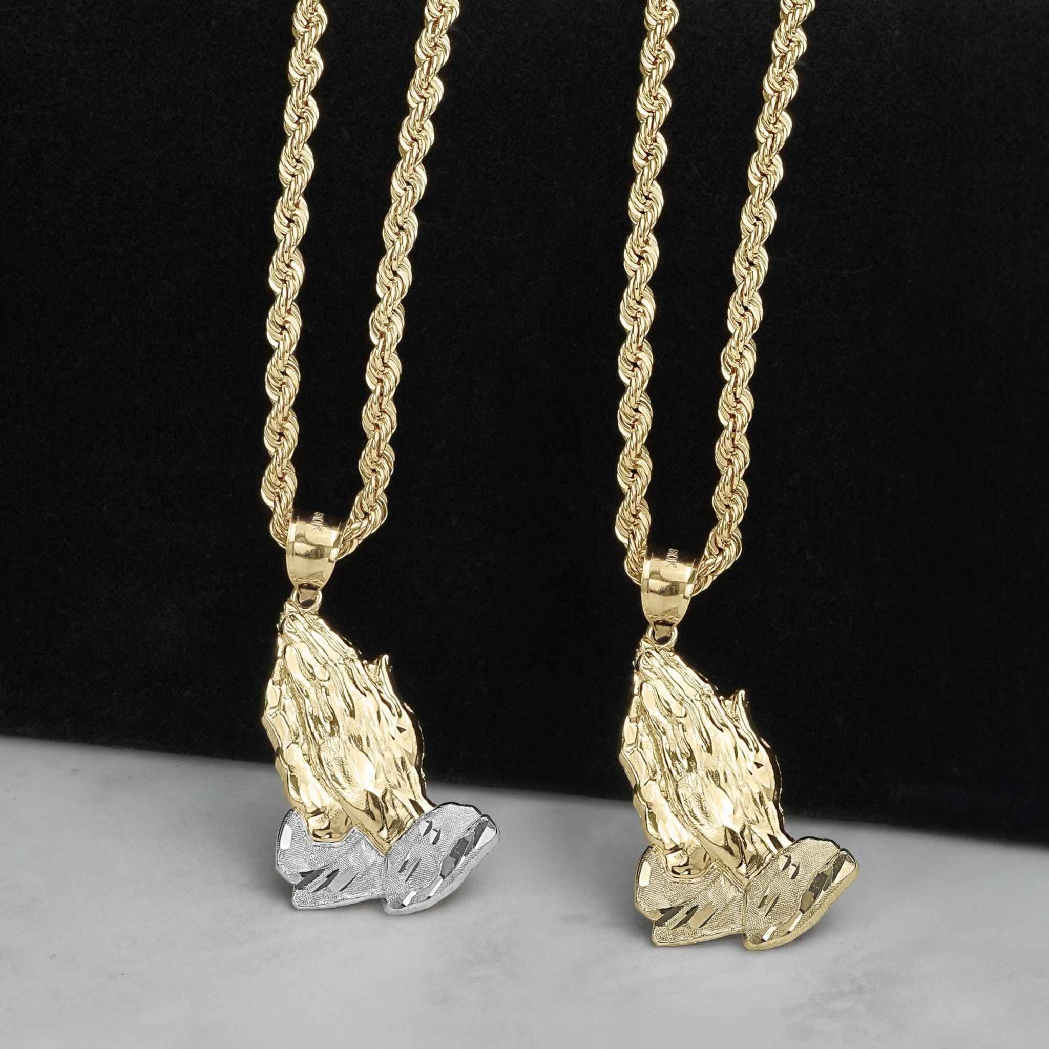 Two-tone and yellow gold praying hands pendants hanging on gold rope chains.