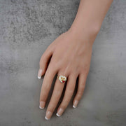 Hand wearing a 10k - 14k gold ring with a red cubic zirconiaon a gray background
