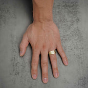 A man's hand displaying a yellow gold square band ring set with sparkling stones.
