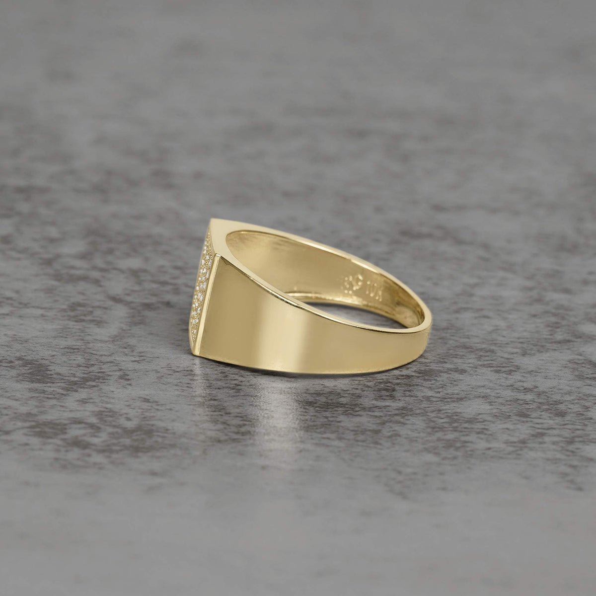 Side view of a men's gold square signet ring on a gray surface.