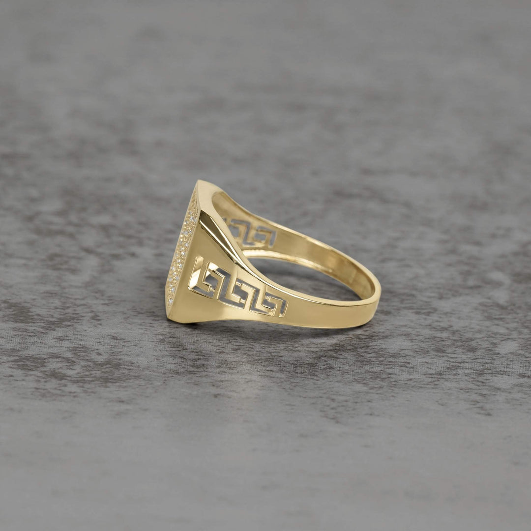 Close-up of hands adjusting two gold Greek key signet rings on a surface.