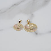 Two tricolor gold round pendants featuring Virgin Mary engravings and sunburst patterns on a white marble surface.