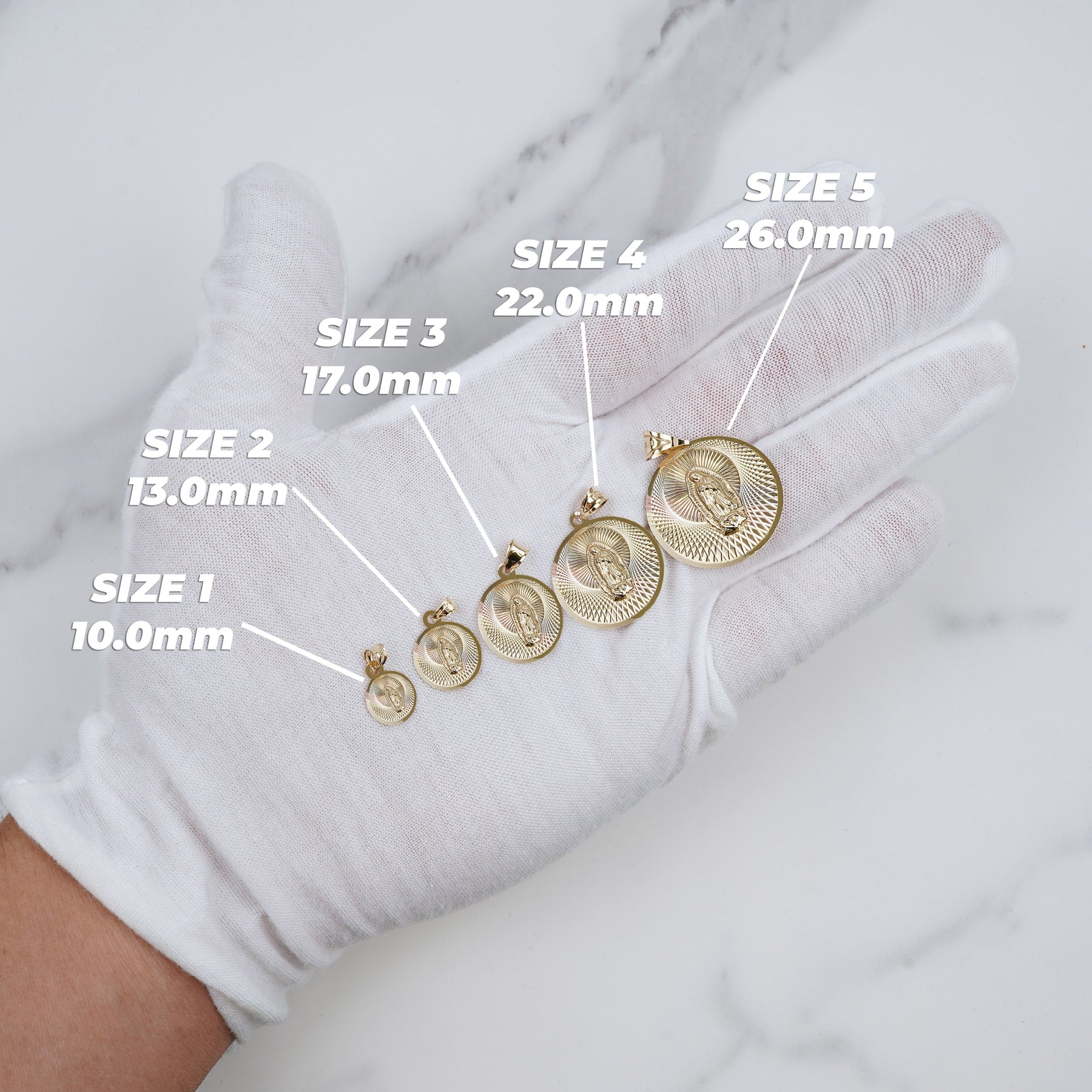 Five varying sizes of tricolor gold Virgin Mary pendants displayed on a white gloved hand with measurement labels.