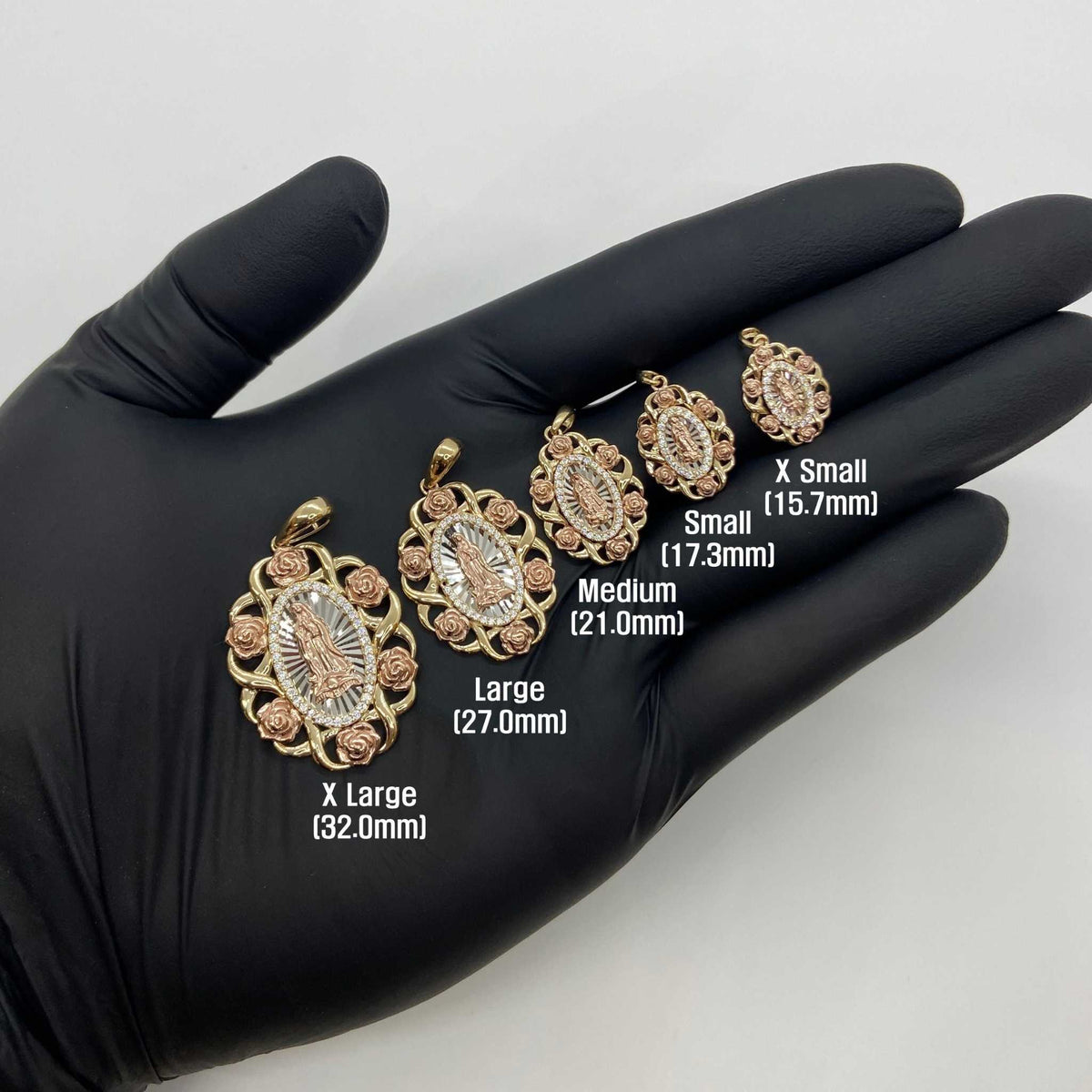 Gloved hand displaying five sizes of tri-color gold Virgin Mary pendant charms from X Small to X Large.
