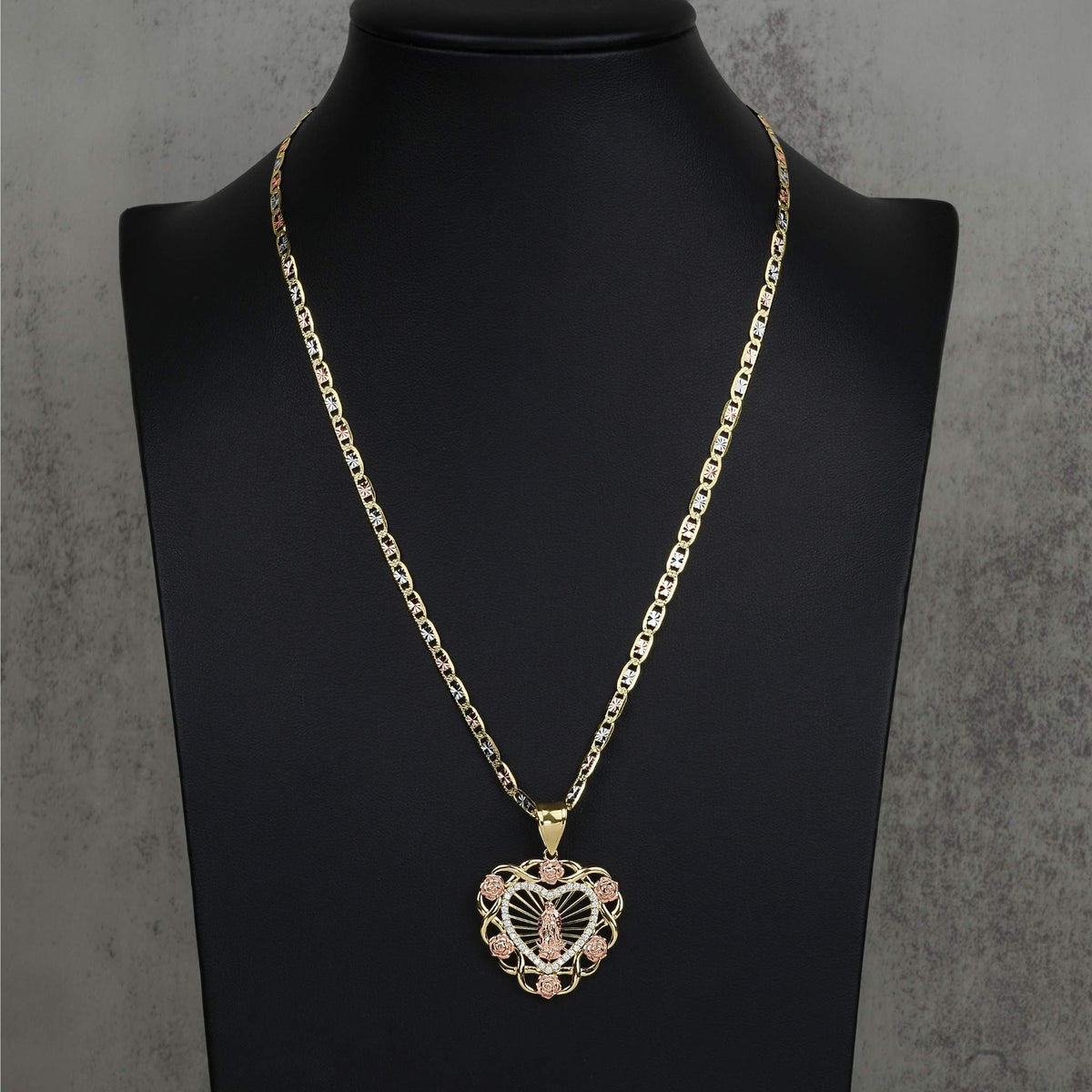 A gold chain necklace with a heart-shaped pendant on a black jewelry bust.