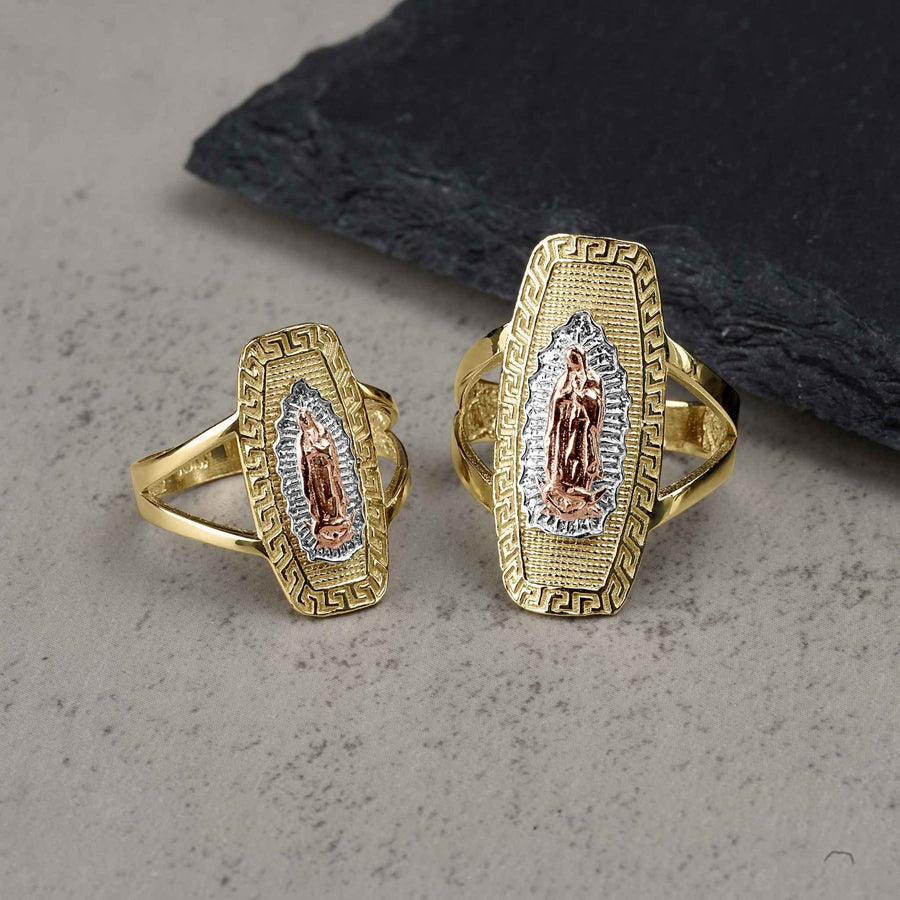 Two sizes of the gold tricolor Virgin Mary rounded rectangle ring on a stone surface.