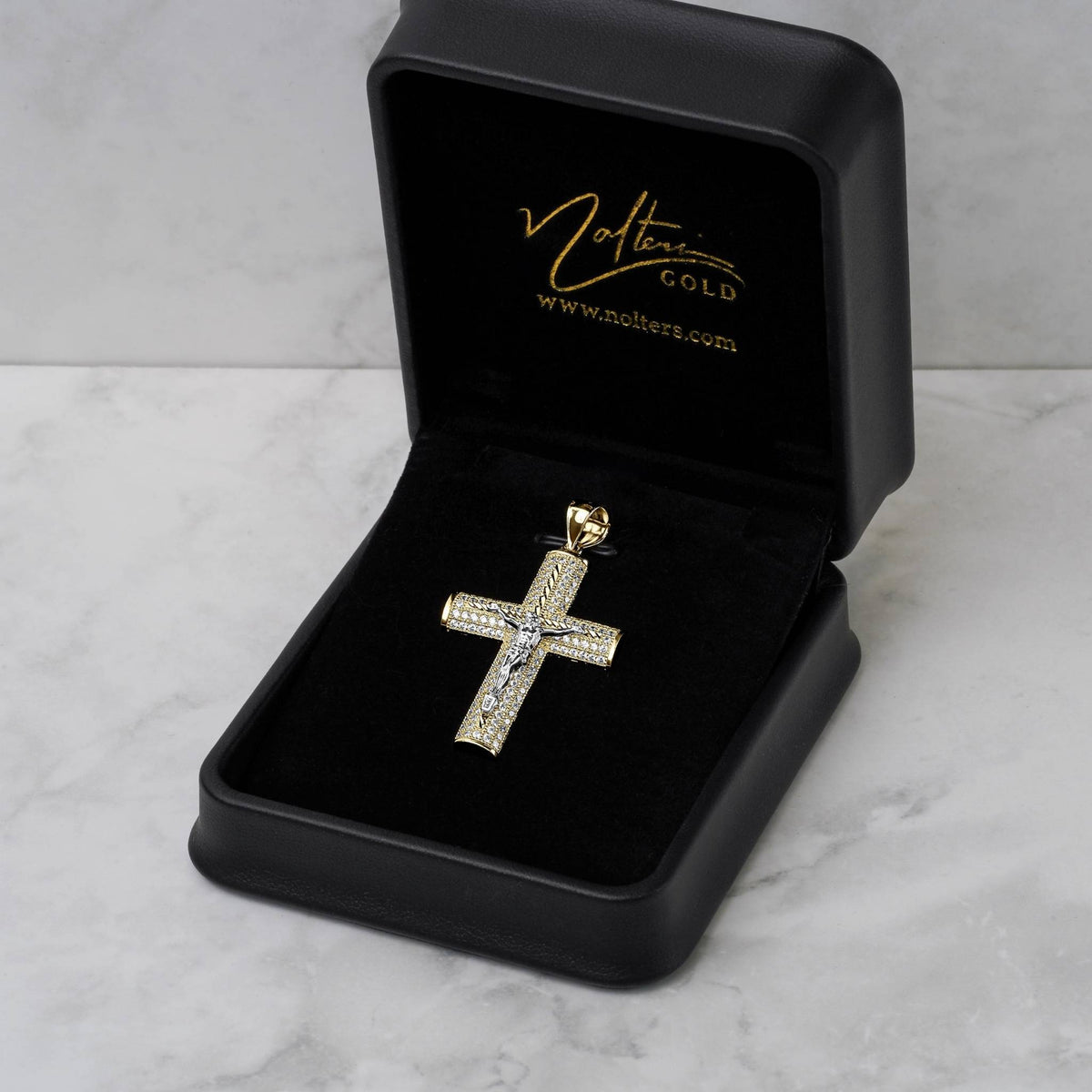 Gold and CZ cross pendant inside an open black jewelry box with gold logo branding.