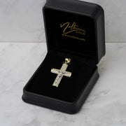 Gold crucifix pendant encrusted with cubic zirconia inside an open black velvet jewelry box.