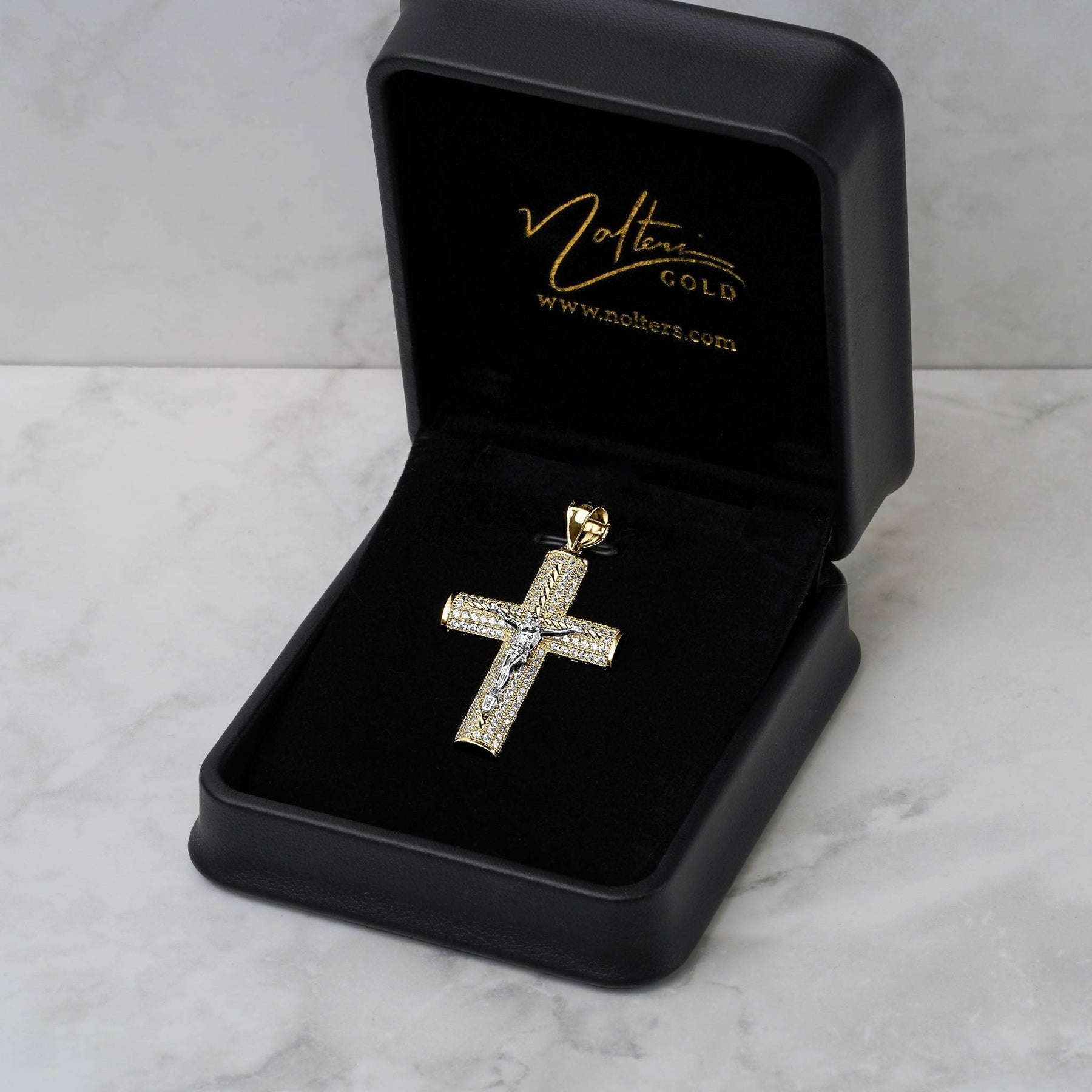Gold crucifix pendant encrusted with cubic zirconia inside an open black velvet jewelry box.