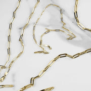 10k and 14k yellow gold fancy paperclip link chains scattered on white marble.