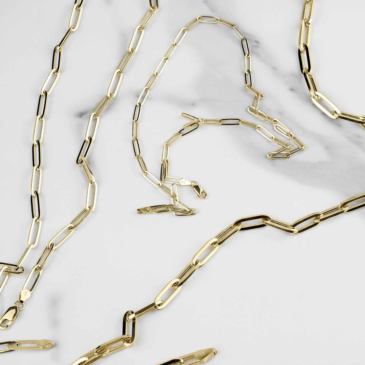 10k and 14k yellow gold fancy paperclip link chains scattered on white marble.