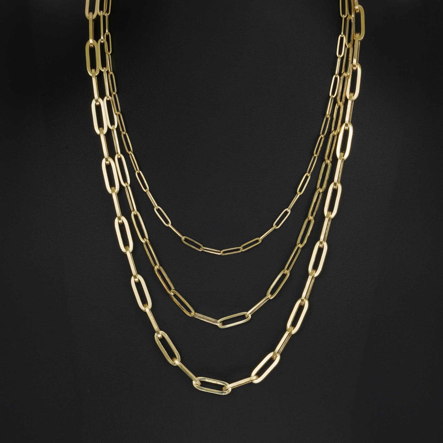 Three 10k and 14k yellow gold fancy paperclip chain necklaces layered on a dark jewelry mannequin bust.