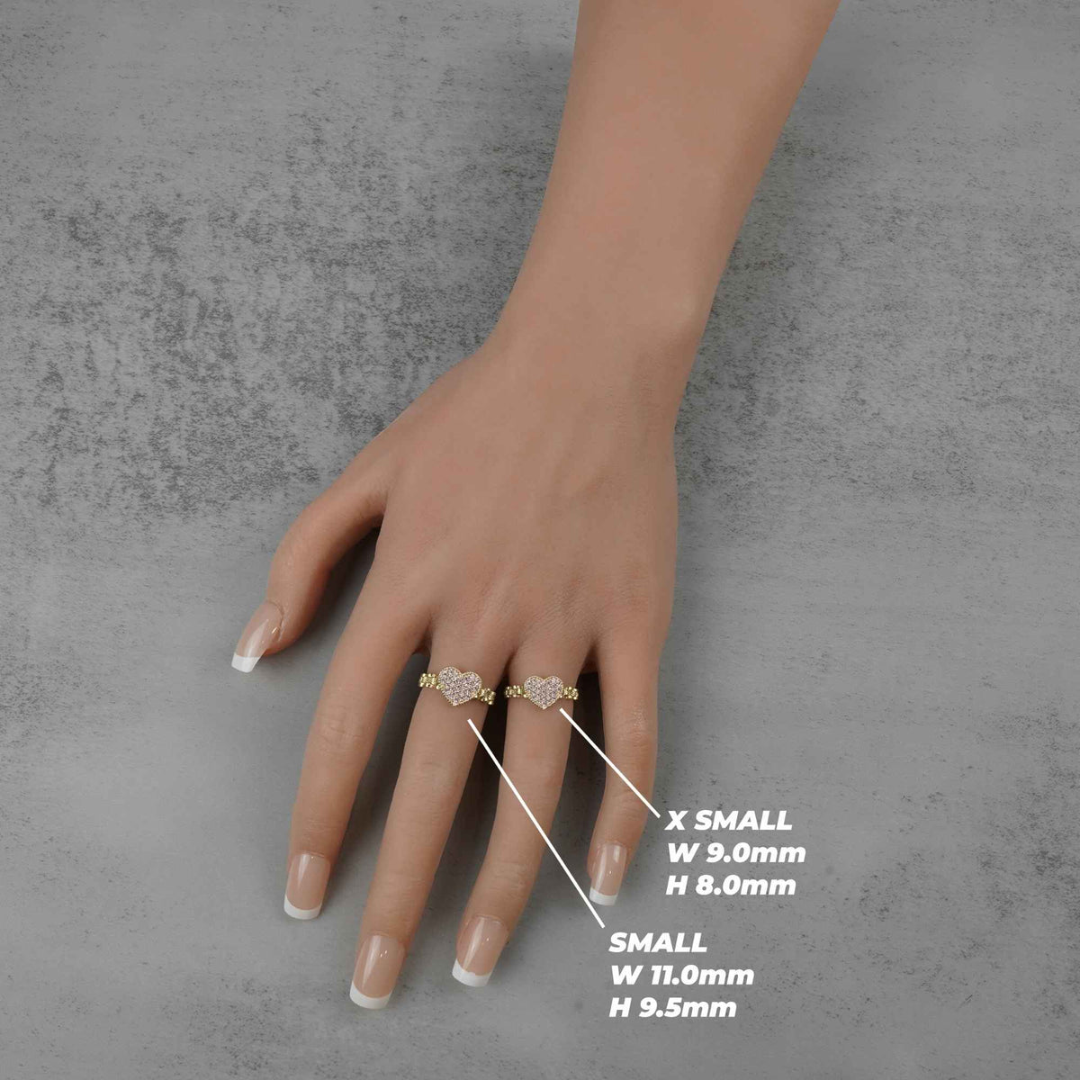 Hand wearing two 10k heart rings with size measurements on a gray background