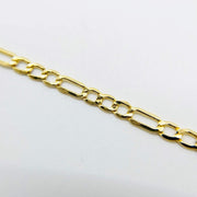 Diagonal close-up of 10k yellow gold Figaro link chain on white background.