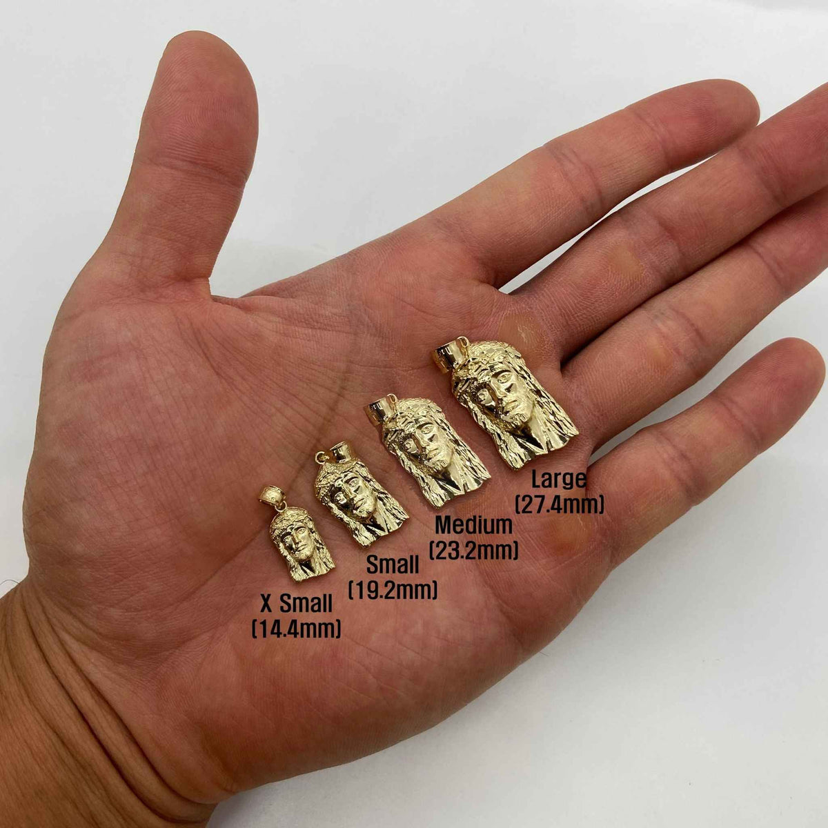 Four sizes of 10k solid gold Jesus Face pendants resting on an open palm.