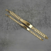 Pair of 10k yellow gold hollow Rollie style ID chain bracelets displayed diagonally on a textured gray background.