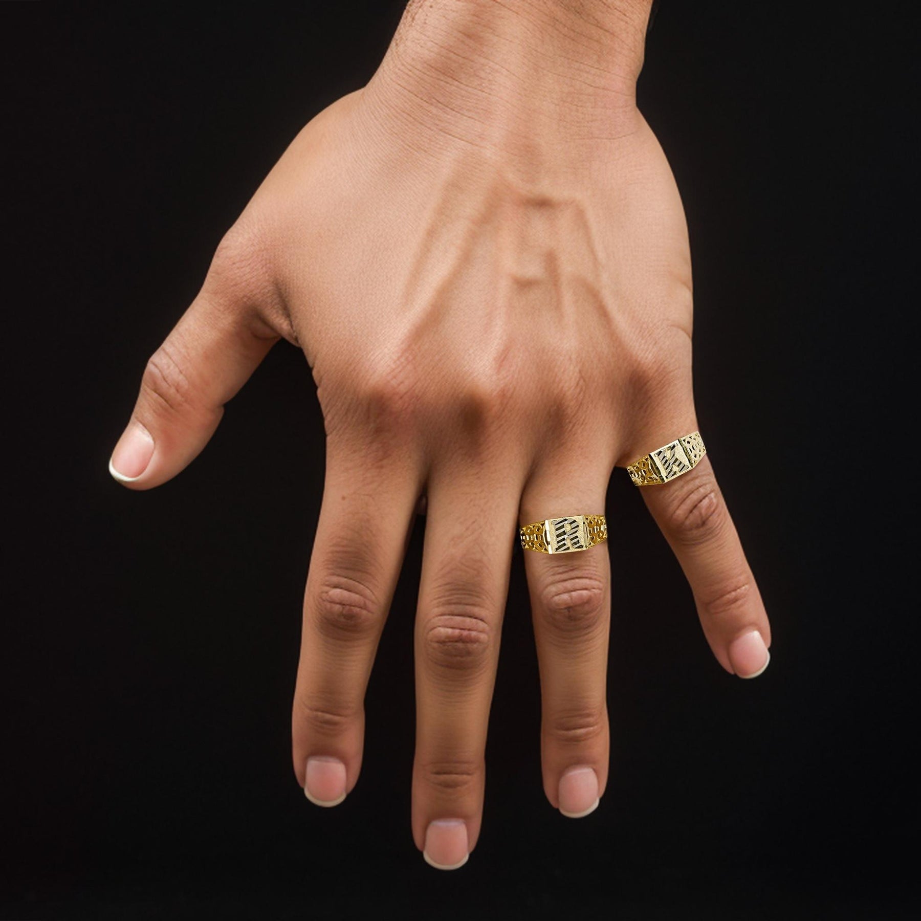 Hand wearing two 10k gold square initial rings against a black background.