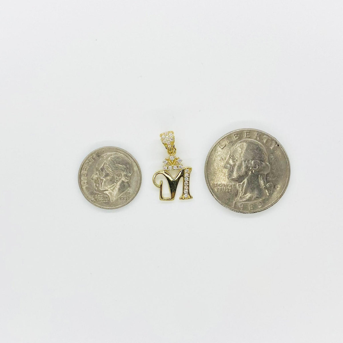 Gold crown initial 'M' pendant placed between two coins for size reference.