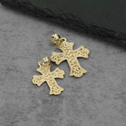 Two textured yellow gold cross pendants resting on a dark gray stone surface.