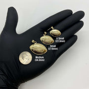 Three gold football pendant sizes held on a gloved hand next to a quarter.