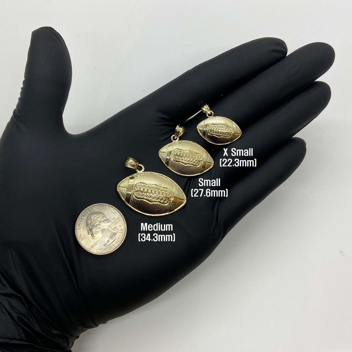 Three gold football pendant sizes held on a gloved hand next to a quarter.