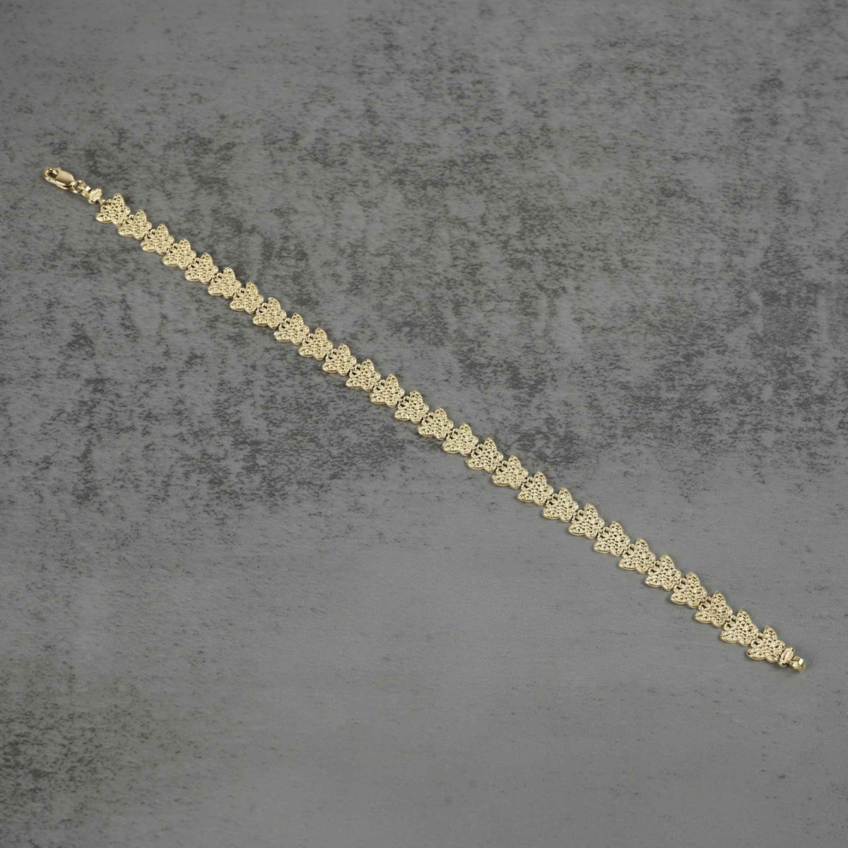 10k gold Forev nugget butterfly link bracelet laid diagonally on a gray surface.