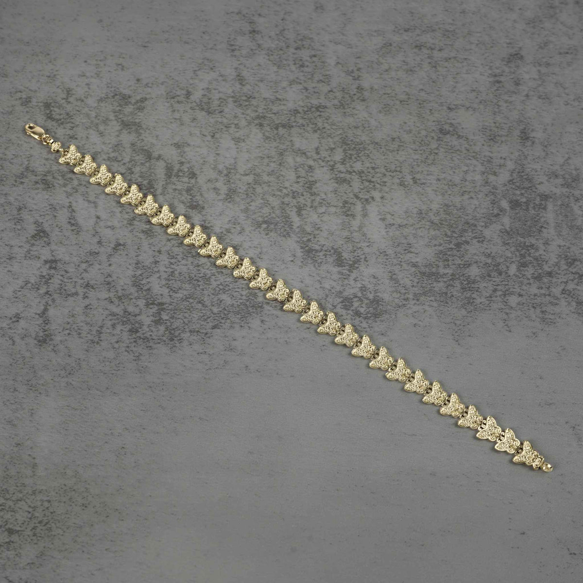 Back view of a 10k gold Forev nugget butterfly link bracelet flat on gray surface.